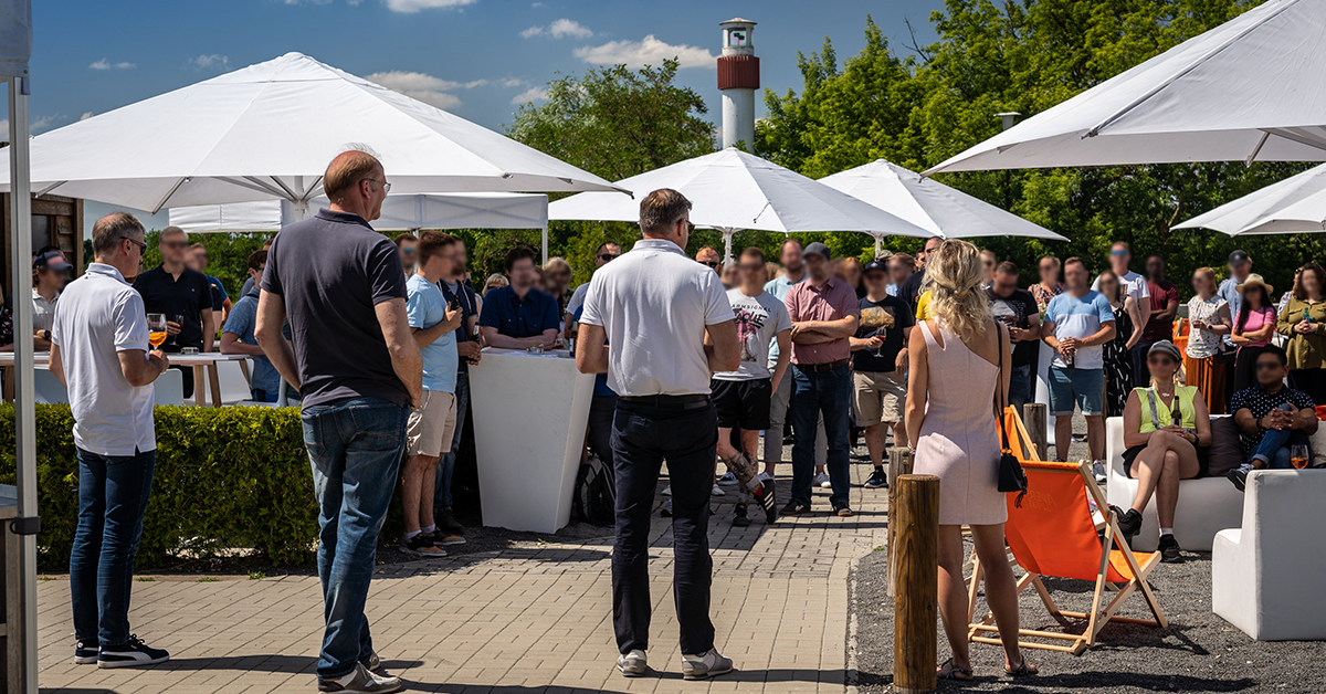 Live-Events wie Firmenfeiern sind ein Highlight im Veranstaltungsjahr. Hier stehen Führungskräfte im Außenbereich der Eventlocation amSee vor zahlreichen Mitarbeitern und begrüßen sie zu einer Firmen-Sommerparty.