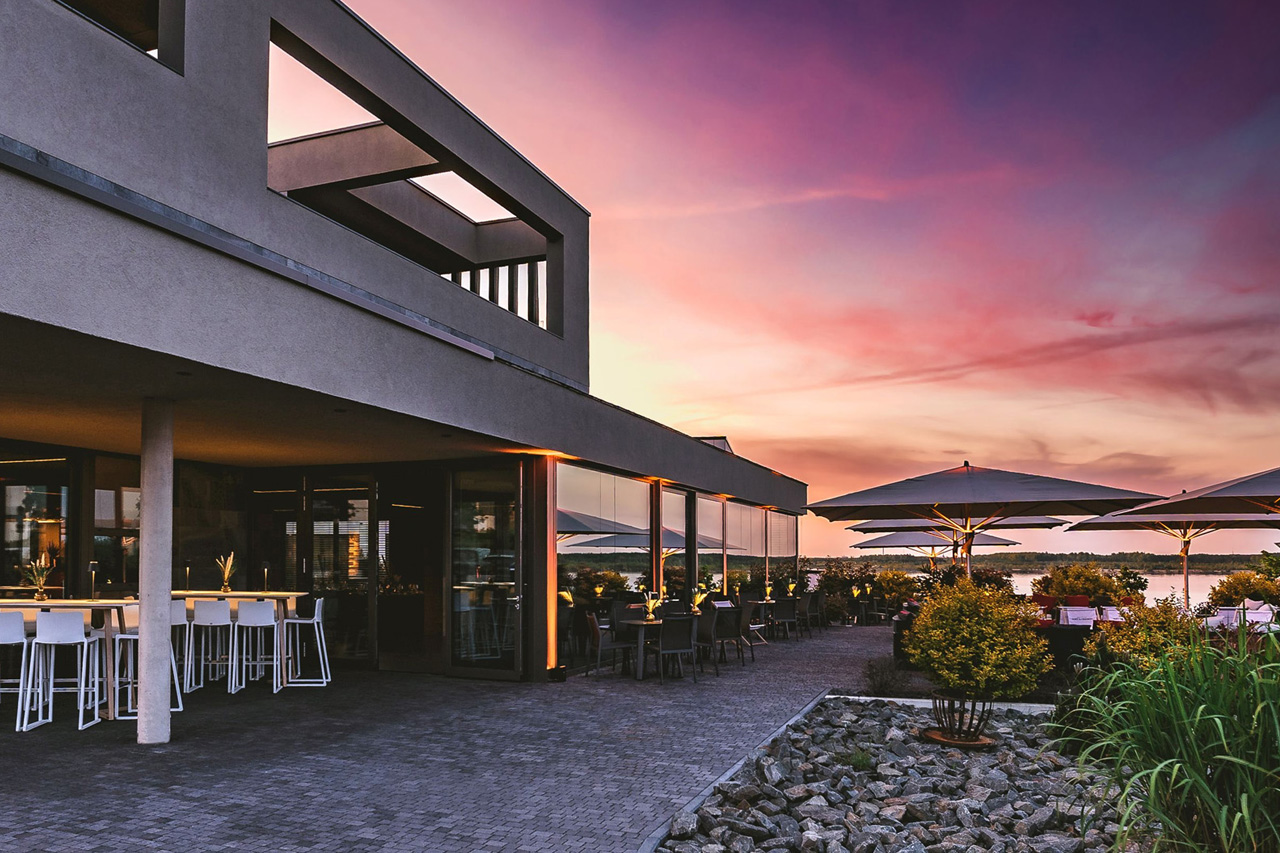 Vordere Terrasse und Haupteingang der LAKESIDE Eventlocation im Abendlicht, Bauhaus-Stil und weiße Möbel.