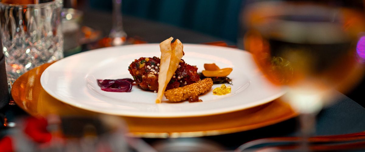 Catering von EVENTFOOD24: feiner Häppchen auf weißem Teller, darunter goldener Platzteller