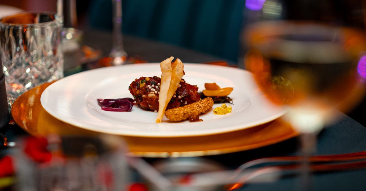 Catering von EVENTFOOD24: feiner Häppchen auf weißem Teller, darunter goldener Platzteller