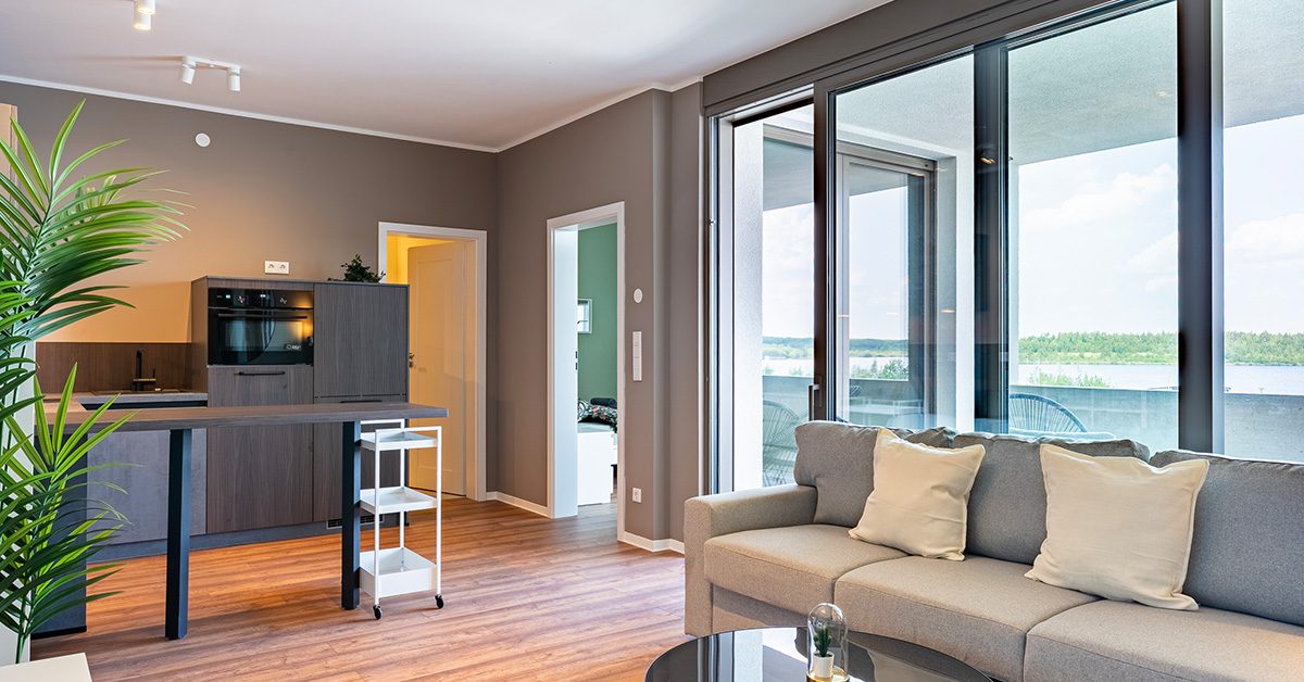 Wohnbereich eines Apartments in der Hafenstraße 6 mit grauem Sofa, Couchtisch und Holzfußboden, im Hintergrund Küchenecke mit dunklen Fronten.