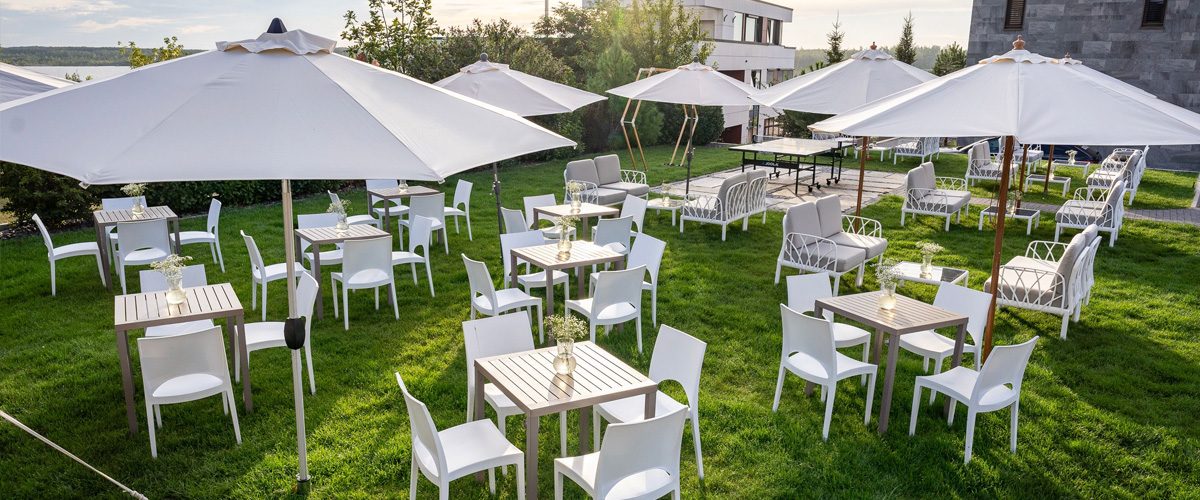 Weiße Möbel stehen auf einem sattgrünen Rasen im Garten der Eventlocation LAKESIDE. Diese und weitere Locations von ALTUS.EVENTS arbeiten daran, nachhaltige Events umzusetzen.