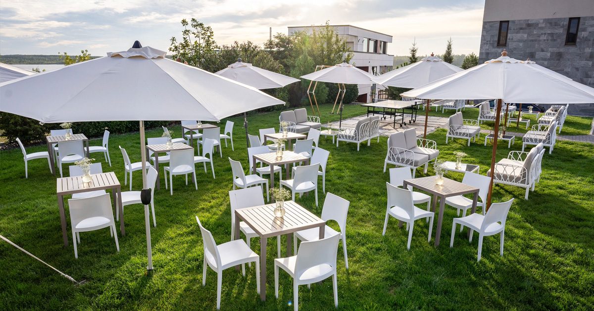 Weiße Möbel stehen auf einem sattgrünen Rasen im Garten der Eventlocation LAKESIDE. Diese und weitere Locations von ALTUS.EVENTS arbeiten daran, nachhaltige Events umzusetzen.